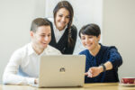 Drei Personen arbeiten gemeinsam an einem Laptop in einer modernen Büroumgebung.