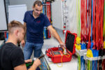 Personen arbeiten an einem Prüfgerät für elektrische Messungen in einem Elektrotechnik-Schulungsraum.