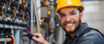 Techniker mit Schutzhelm und Schutzbrille arbeitet an einer elektrischen Schaltanlage in einer Werkstatt