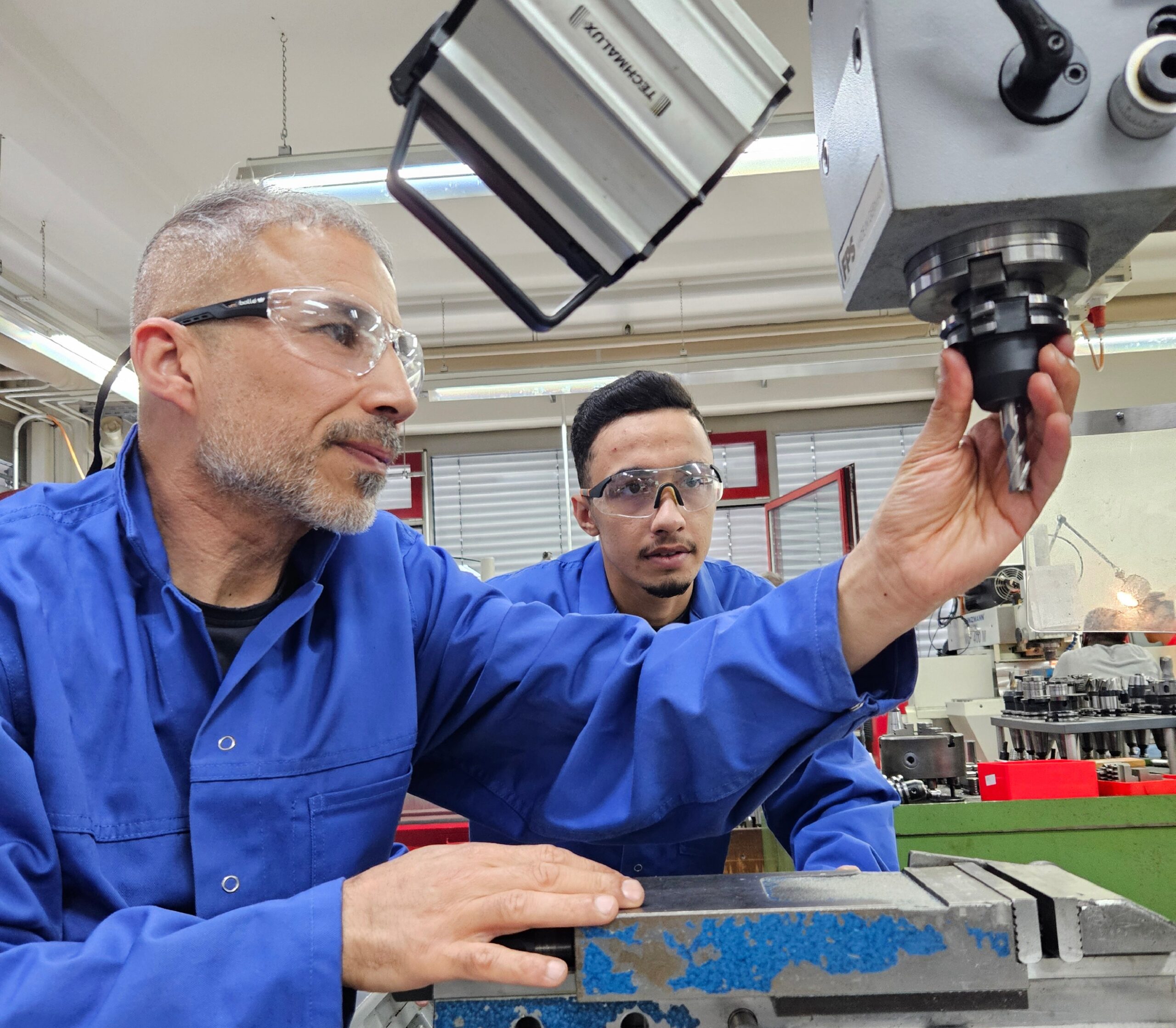 Zwei Teilnehmende der Qualifizierungsmaßnahme Fachkraft in der Produktion prüfen gemeinsam ein Werkzeug an einer Fräsmaschine