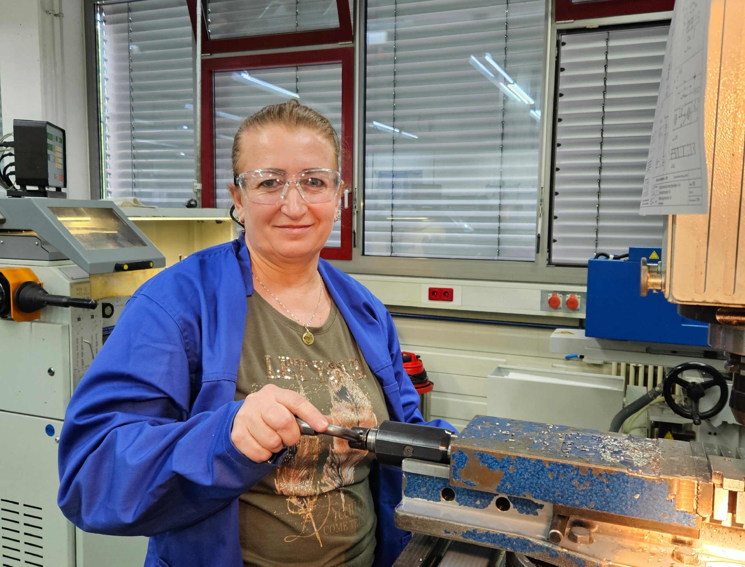Lächelnde Teilnehmerin der Qualifizierungsmaßnahme Fachkraft in der Produktion bei der Arbeit an einer Werkzeugmaschine