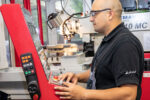 Person mit Schutzbrille bedient das Steuerpult einer CNC-Fräsmaschine in einer Fertigungsumgebung.